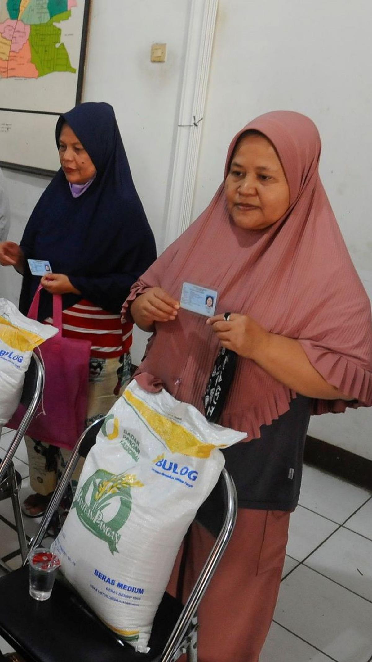 Warga memegang kartu identitas miliknya saat difoto oleh petugas usai menerima bansos beras Bulog.