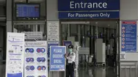 Petugas keamanan berdiri di samping pengingat protokol kesehatan COVID-19 yang ditempatkan di pintu masuk Bandara Internasional Manila, Rabu (17/3/2021). Kedatangan penumpang di bandara internasional Manila telah dibatasi maksimal 1.500 per hari antara 18 Maret hingga 19 April. (AP Photo/Aaron Favil