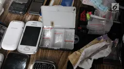 Sejumlah telepon genggam dan paket narkoba yang berhasil diamankan petugas saat penggerebekan di Kampung Ambon, Cengkareng, Jakarta, Rabu (24/1). Petugas mengamankan sabu, ganja, bong, timbangan. (Liputan6.com/Arya Manggala)