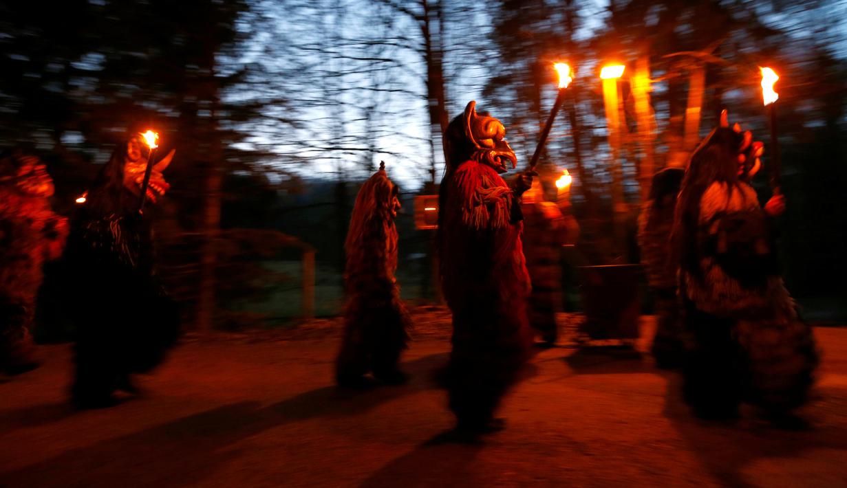 Sejumlah peserta mengenakan kostum iblis membawa obor saat mengikuti parade tardisional Perchtenlauf di Osterseeon dekat Munchen, Jerman (17/12). Acara ini bertujuan untuk mengusir hantu-hantu musim dingin. (Reuters/Michaela Rehle)