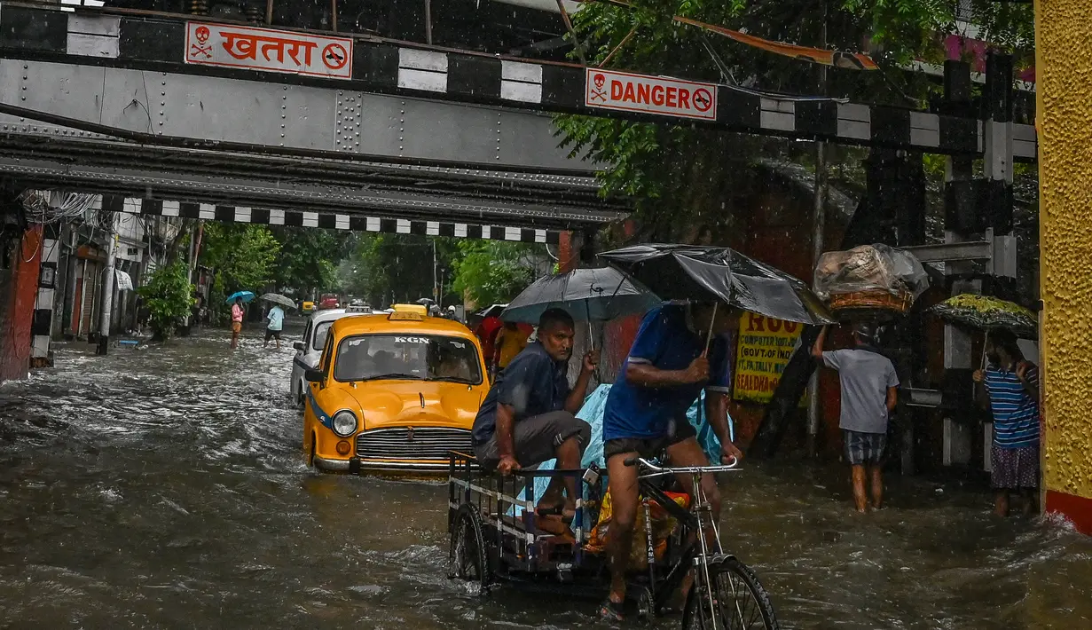 Komuter berjalan di sepanjang jalan yang tergenang air setelah hujan lebat di Kolkata (20/9/2021). Hujan dilaporkan dipicu oleh sirkulasi siklon yang terbentuk di atas Teluk Benggala. (AFP/Dibyangshu Sarkar)