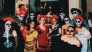 Wajahnya juga dihiasi dengan riasan calavera serupa, dengan sentuhan artistik bunga mawar yang mencerminkan keterkaitan pasangan ini dalam tema mereka. Latarnya yang dipenuhi bunga oranye khas Dia de los Muertos memberikan suasana meriah dan penuh warna, menghidupkan semangat perayaan tradisional tersebut. [@itsmebcl].
