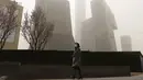 Seorang wanita melewati dekat gedung pencakar langit di Central Business District saat badai pasir di Beijing (28/3/2021). Sebelumnya Badai pasir menyapu Beijing, China pada Senin (15/3/2021) pagi.  (AP Photo/Ng Han Guan)
