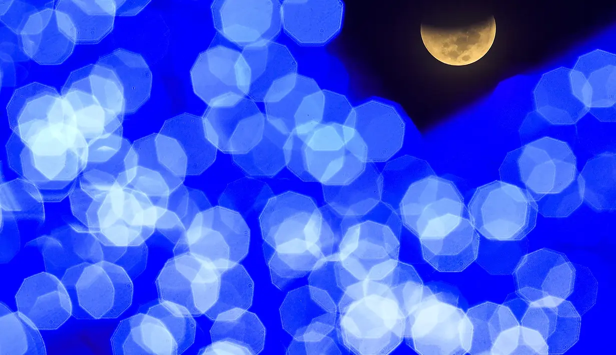 Terlihat melewati lampu Natal, bayangan bumi mulai menutupi bulan saat gerhana bulan, di alun-alun di Caracas, Venezuela, Selasa dini hari, 8 November 2022. Fenomena gerhana bulan total terjadi pada 8 November 2022 di berbagai negara. (AP Photo/Matias Delacroix)