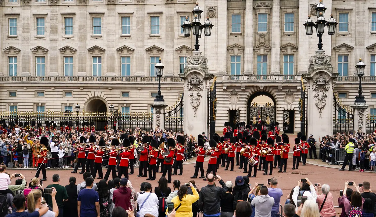 Orang-orang menyaksikan prosesi pergantian penjaga di Istana Buckingham, London, Senin (23/8/2021). Pergantian pasukan jaga yang dilengkapi dengan alat musik lengkap ala marching band tersebut berlangsung untuk pertama kalinya sejak dimulainya pandemi corona Covid-19. (AP Photo/Alberto Pezzali)