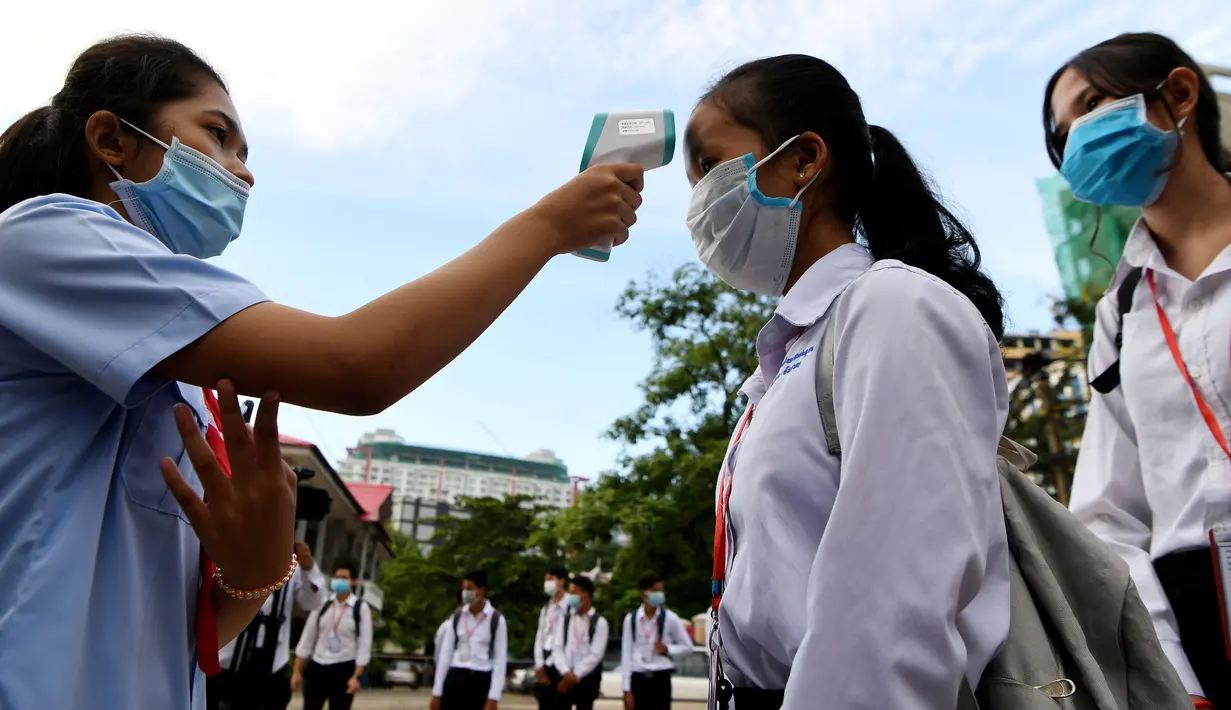 Siswa yang mengenakan masker diukur suhu tubuhnya setibanya di kompleks sekolah mereka ketika sekolah dibuka kembali di Phnom Penh, Senin (7/9/2020). Sekolah-sekolah di Kamboja dibuka kembali pada Senin (7/9) setelah enam bulan ditutup akibat COVID-19. (TANG CHHIN Sothy /AFP)