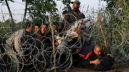 Sejumlah imigran Suriah merangkak untuk melewati pagar berduri di wilayah Hungaria dekat perbatasan Serbia, wilayah Roszke, Kamis (27/8/2015). Hungaria berencana untuk memperketat perbatasan bagian selatannya dari para pengungsi. (REUTERS/Bernadett Szabo)