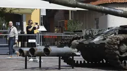 Seorang wanita menggunakan ponselnya mengabadikan tank Rusia yang rusak dan terbakar di Castle Square, di Warsawa, Polandia (27/6/2022). Pihak berwenang Ukraina mengumumkan bahwa ada rencana untuk pameran serupa di ibu kota Eropa lainnya seperti Berlin, Paris, Madrid dan Lisbon. (Foto AP/Michal Dyjuk)