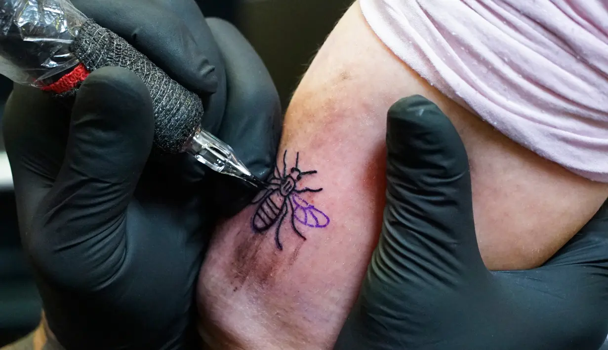 Seorang seniman tato menyelesaiakan pembuatan tato bergambar lebah di Manchester (28/5). Sebelumnya, serangan bom yang terjadi saat konser Ariana Grande menyebabkan 22 orang tewas dan melukai 119 lainnya. (AP Photo/Mstyslav Chernov)