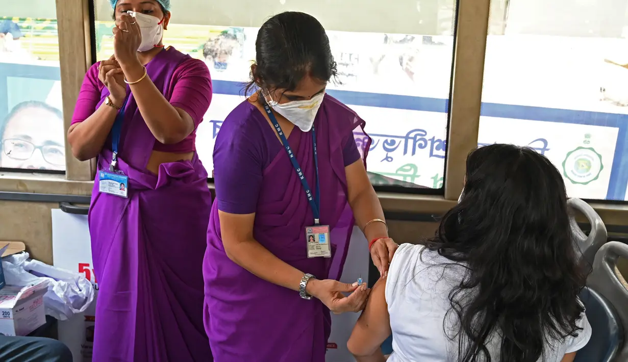 Petugas kesehatan menyuntik seorang pekerja dengan vaksin Covid-19 Covishield di dalam bus penumpang yang diubah menjadi pusat vaksinasi keliling di Kolkata, Kamis (3/6/2021). India telah menderita pandemi yang menghancurkan sejak April, dan baru-baru ini mulai mereda. (Dibyangshu SARKAR/AFP)