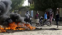 Orang-orang melakukan protes dekat kobaran api di N'Djamena, Chad, Selasa (27/4/2021). Ribuan orang melakukan protes dan dua orang tewas dalam demonstrasi menentang aturan dewan militer transisi yang dipimpin putra Presiden Idriss Deby Itno yang terbunuh minggu lalu. (AP Photo/Sunday Alamba)