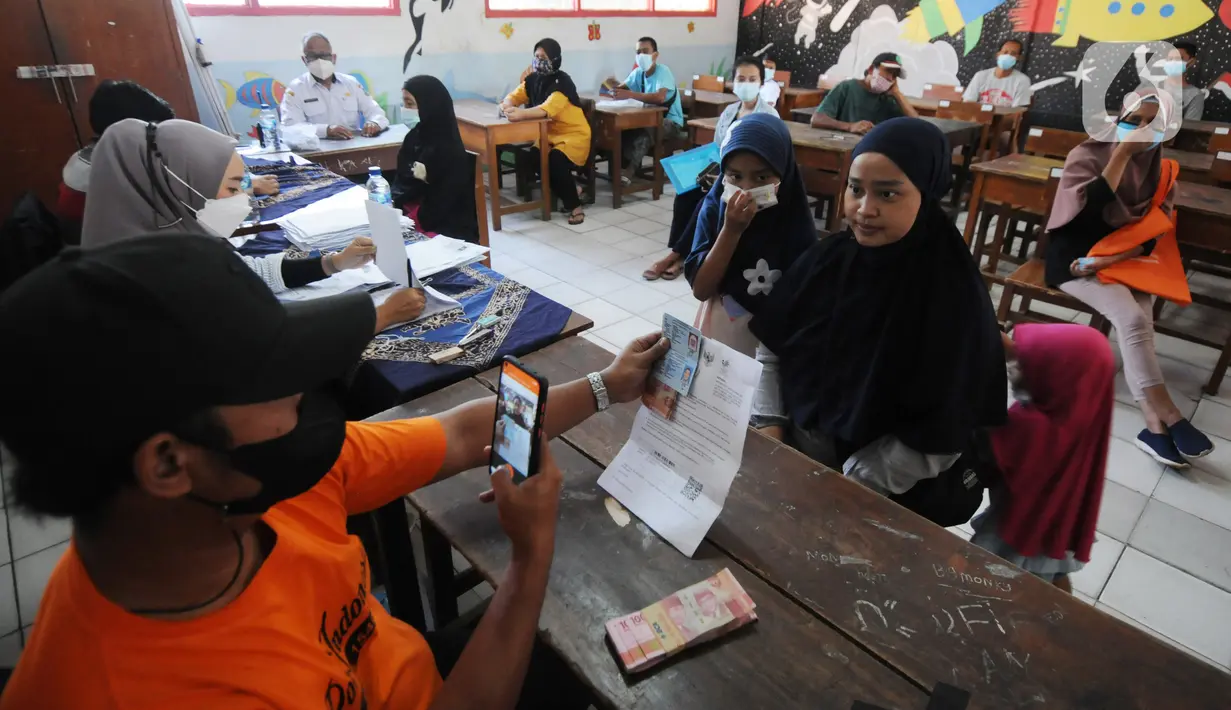 Petugas memotret warga penerima Bantuan Sosial Tunai (BST) di SDN Pondok Cabe Udik 03, Tangerang Selatan, Rabu (28/07/2021). Lebih dari dari 1800 warga mendapatkan BST yang dirapel dua bulan sekaligus dengan total Rp600ribu. (merdeka.com/Arie Basuki)