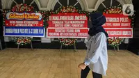 Seorang wanita berjalan dekat karangan bunga di halaman Kantor PT Asuransi Jiwasraya (Persero), Jakarta, Selasa (15/12/2020). Karangan bunga tersebut berisi ucapan dukungan kepada manajemen baru Jiwasraya dalam penyelamatan polis melalui program restrukturisasi. (Liputan6.com/Faizal Fanani)