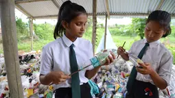 Siswa India memasukkan kantong plastik ke dalam botol untuk membuat "batu bata ramah lingkungan" di sekolah Forum Akshar di desa Pamohi, Guwahati, 20 Mei 2019. 110 murid sekolah ini harus membawa 20 item sampah plastik per minggu yang dikumpulkan dari rumah atau area sekitar mereka. (Biju BORO/AFP)
