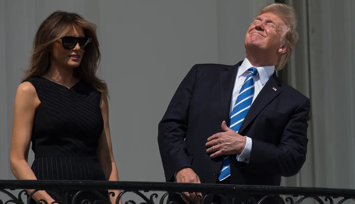 Presiden AS Donald Trump bersama Ibu Negara, Melania Trump menyaksikan fenomena langka gerhana matahari dari balkon Gedung Putih di Washington, Senin (21/8). Trump tampak menatap langsung ke arah matahari dengan mata telanjang. (NICHOLAS KAMM/AFP)