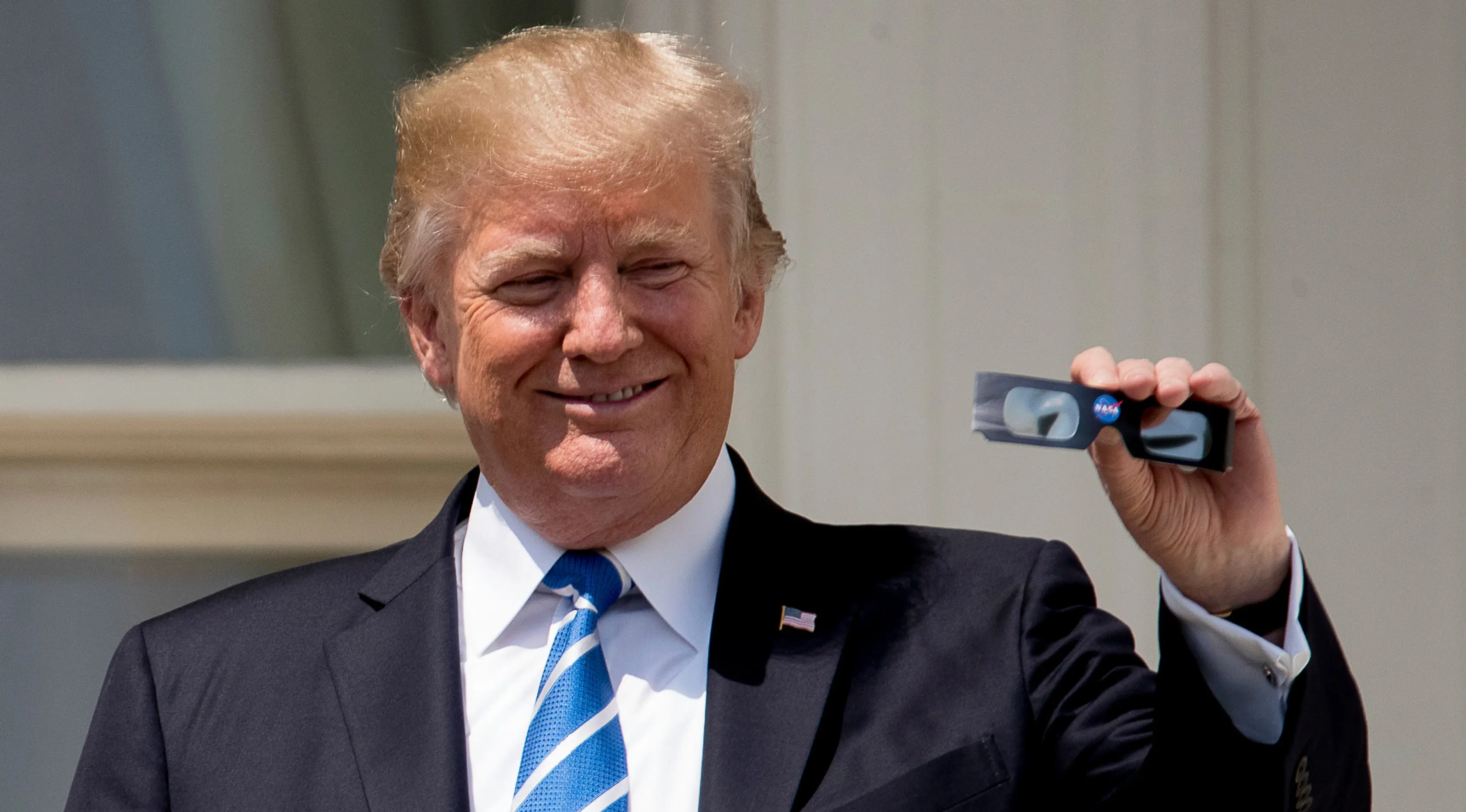 Presiden AS Donald Trump memperlihatkan kacamata pelindung sebelum menyaksikan  gerhana matahari dari balkon Gedung Putih di Washington, Senin (21/8). Gerhana matahari total di Amerika Serikat terlihat langsung di 14 negara bagian (AP Photo/Andrew Harnik)