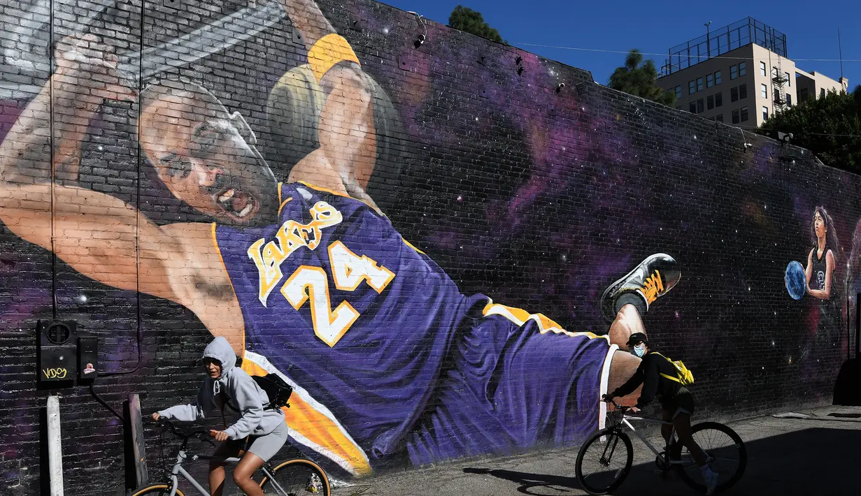 Pesepeda melintas di depan lukisan mural bintang LA Lakers, Kobe Bryant di Los Angeles, California, Selasa (26/1/2021). Lukisan dibuat untuk mengenang 1 tahun tragedi kecelakaan helikopter yang menewaskan Kobe Bryant bersama putrinya, Gianna. (Getty Images via AFP/Harry How)