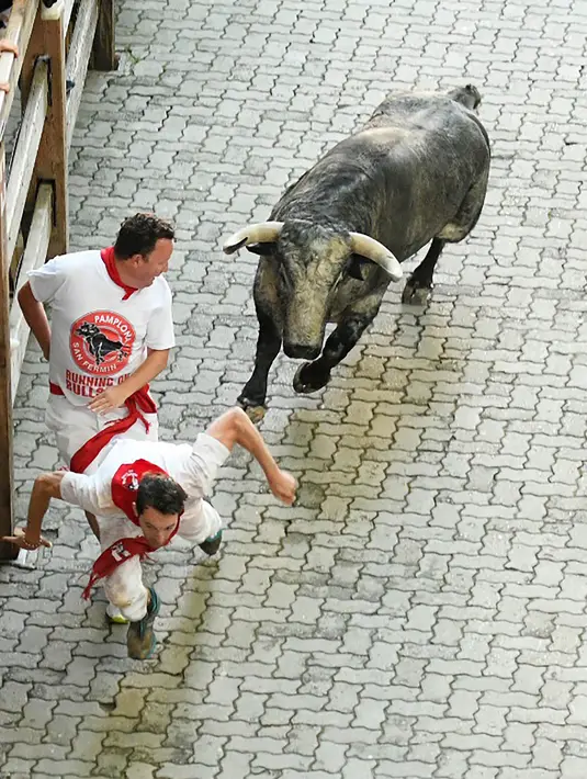 Dua orang peserta berusaha menghindar dari serudukan banteng  selama hari ketiga Festival San Fermin di Pamplona, Spanyol utara, (9/7). (AFP Photo/Jose Jordan)