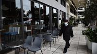 Seorang pria berjalan melewati kafe dan restoran yang tutup di Thessaloniki, Yunani, Selasa (16/11/2021). Pemilik restoran, kafe, dan bar melakukan pemogokan selama 24 jam, memprotes aturan terkait Covid-19 dan biaya energi yang tinggi. (Sakis MITROLIDIS / AFP)