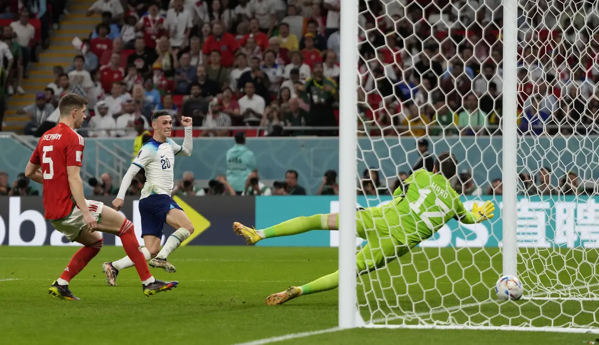 Gelandang Inggris Phil Foden (tengah) mencetak gol kedua untuk timnya melewati kiper Wales Danny Ward pada pertandingan terakhir Grup B di Ahmad bin Ali Stadium, Rabu (30/11/2022) dini hari WIB. Setelah babak pertama yang buruk dengan hasil imbang tanpa gol, Inggris memulai babak kedua dengan penampilan penuh semangat. (AP Photo/Frank Augstein)