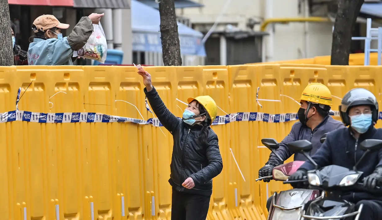 Seorang wanita (kiri) menjual barang dari balik penghalang saat lockdown sebagai tindakan terhadap virus corona COVID-19 di Distrik Jing'an, Shanghai, China, 31 Maret 2022. (Hector RETAMAL/AFP)