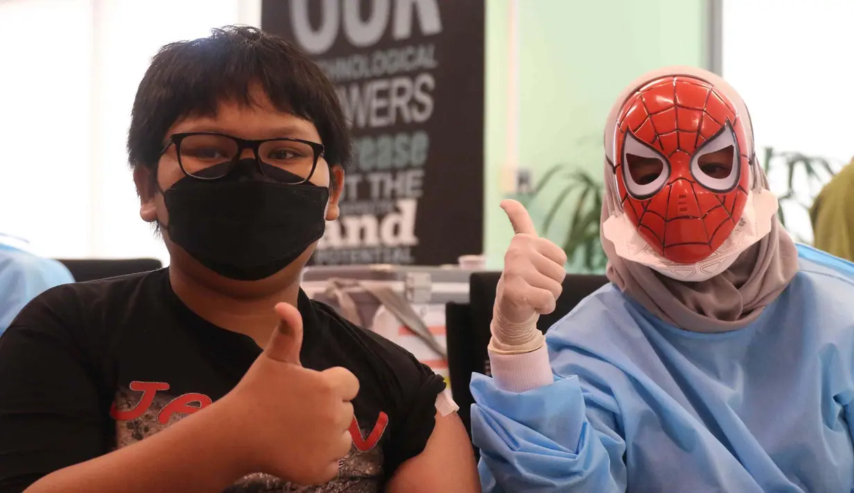 Seorang anak berpose dengan petugas medis yang mengenakan topeng superhero usai mengikuti vaksinasi kedua di Gedung  OJK, Jakarta, Minggu (16/01/2022). Bertemakan superhero untuk menghilangkan stigma menakutkan bagi anak-anak. (Liputan6.com/Angga Yuniar)