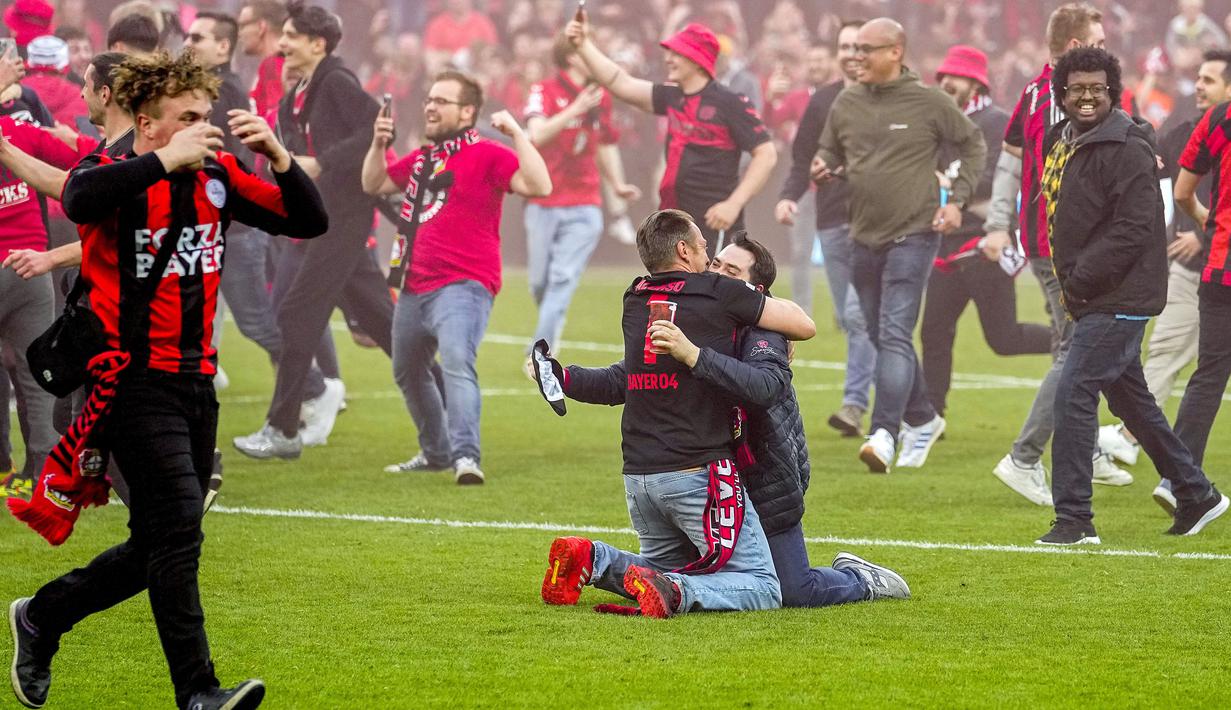 Dua orang suporter Bayer Leverkusen berpelukan saat merayakan keberhasilan timnya menjuarai Liga Jerman 2023/2024 setelah mengalahkan Werder Bremen di BayArena, Leverkusen, Jerman, Senin (15/04/2024) WIB. (AP Photo/Martin Meissner)