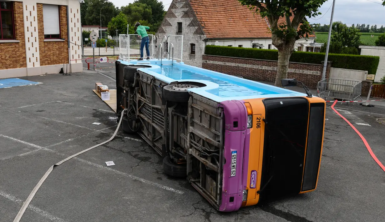 Seorang pria bekerja pada bus kota yang diubah menjadi kolam renang di Gosnay, Prancis Utara pada 15 Juli 2019. Karya seorang seniman Prancis, Benedetto Bufalino ini merupakan bus yang sudah dipensiunkan alias tak layak pakai untuk mengaspal di jalanan kota. (DENIS CHARLET / AFP)
