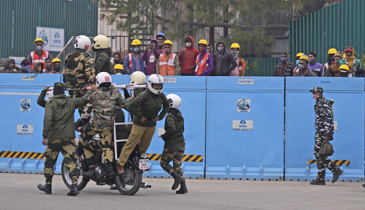 Pekerja menyaksikan pasukan pertahanan berlatih untuk parade Hari Republik mendatang di perbukitan Raisina, pusat kekuasaan pemerintah, di New Delhi, India (17/1/2022). India akan merayakan Hari Republik pada 26 Januari. (AP Photo/Manish Swarup)