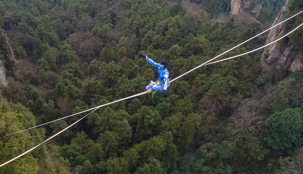 Kontestan berpakaian karakter Avatar bergaya saat melintasi slackline di Pegunungan Huangshizhai di Zhangjiajie, Hunan, China, Minggu (23/12). Pemandangan tersebut memberi sensasi bukit-bukit yang melayang, persis di film Avatar. (STR/AFP)