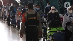 Aparat kepolisian mengamati rombongan jemaah umrah saat tiba di Bandara Soekarno Hatta, Tangerang, Selasa (29/12/2020). Rombongan jemaah umrah yang baru tiba di Indonesia tersebut diarahkan untuk melakukan karantina di tempat yang telah disediakan oleh pemerintah. (Liputan6.com/Angga Yuniar)