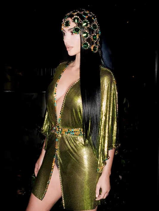Kaftan yang digunakan berbahan mesh metalik hijau limau dan merah berhiaskan kristal di sepanjang tepi dan ikat pinggang. Gaun vintage dari Rabanne ini ia padukan penutup kepala berantai dengan kristal yang senadar serta rambut hitam lurus yang jatuh hingga pinggang. [@kimkardashian]