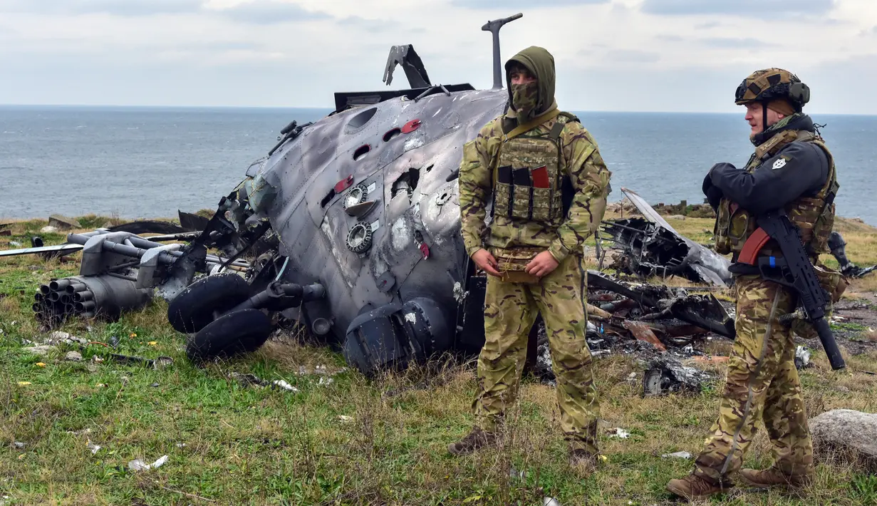 Tentara Ukraina berdiri dengan latar belakang helikopter militer Rusia yang rusak di Pulau Ular, Laut Hitam, Ukraina, 18 Desember 2022. Pasukan Rusia menduduki pulau itu pada awal-awal invasinya ke Ukraina, namun akhirnya mundur beberapa bulan kemudian. (AP Photo/Michael Shtekel)