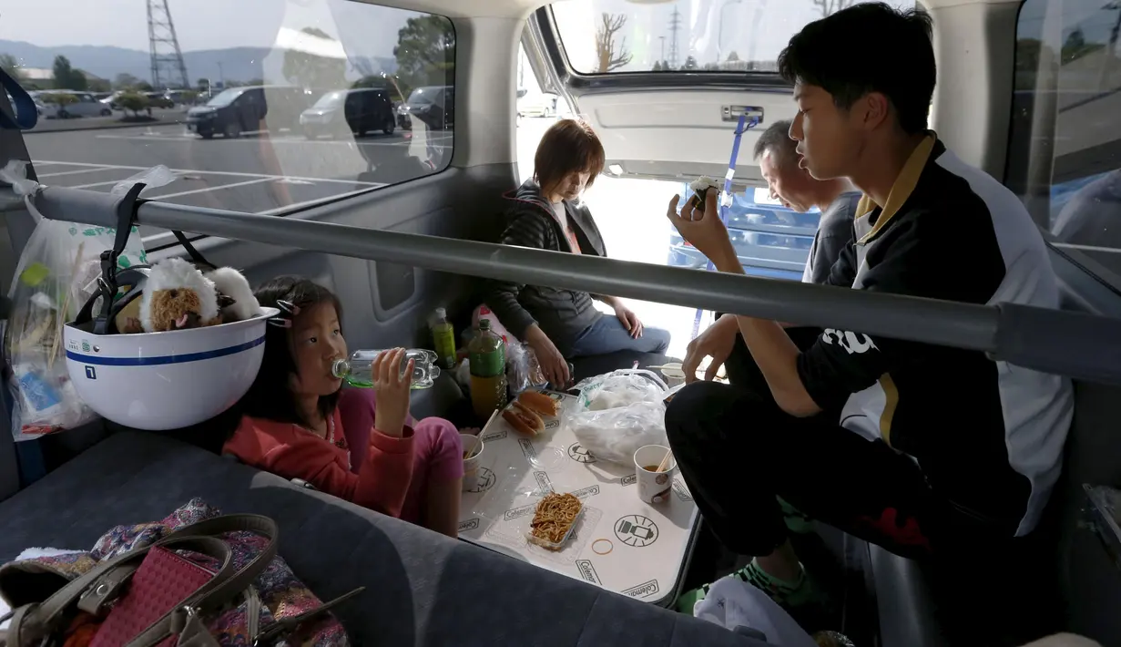 Sebuah keluarga menikmati makanan di dalam mobil mereka di kota Mashiki, prefektur Kumamoto, Jepang, 17 April 2016. Gempa yang terjadi pada Kamis (14/4) malam membuat banyak warga lebih memilih mengungsi dan tidur di mobil mereka sendiri. (Reuters/Kyodo)