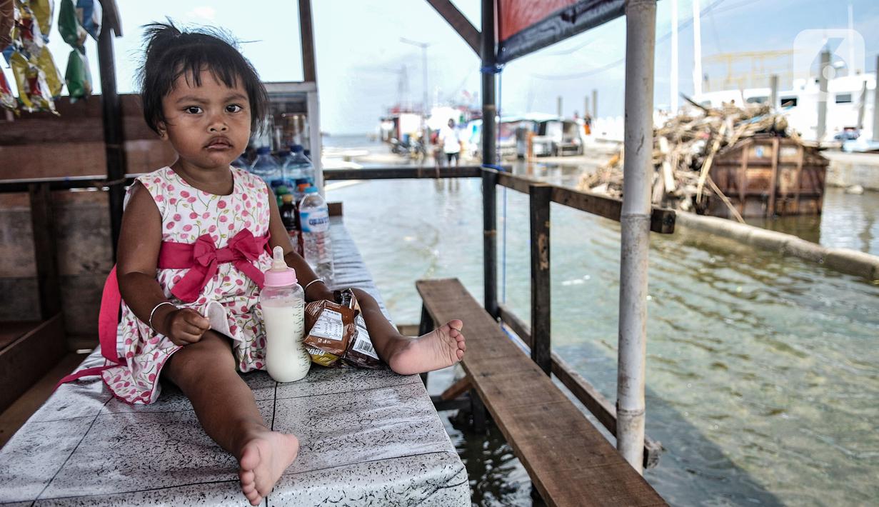 Seorang anak duduk di meja warung saat banjir rob di Pelabuhan Kali Adem, Muara Angke, Jakarta, Kamis (22/10/2020). Banjir akibat air pasang dengan ketinggian mencapai 30 cm tersebut telah merendam kawasan Pelabuhan Kali Adem dan sudah berlangsung selama lima hari. (merdeka.com/Iqbal S. Nugroho)