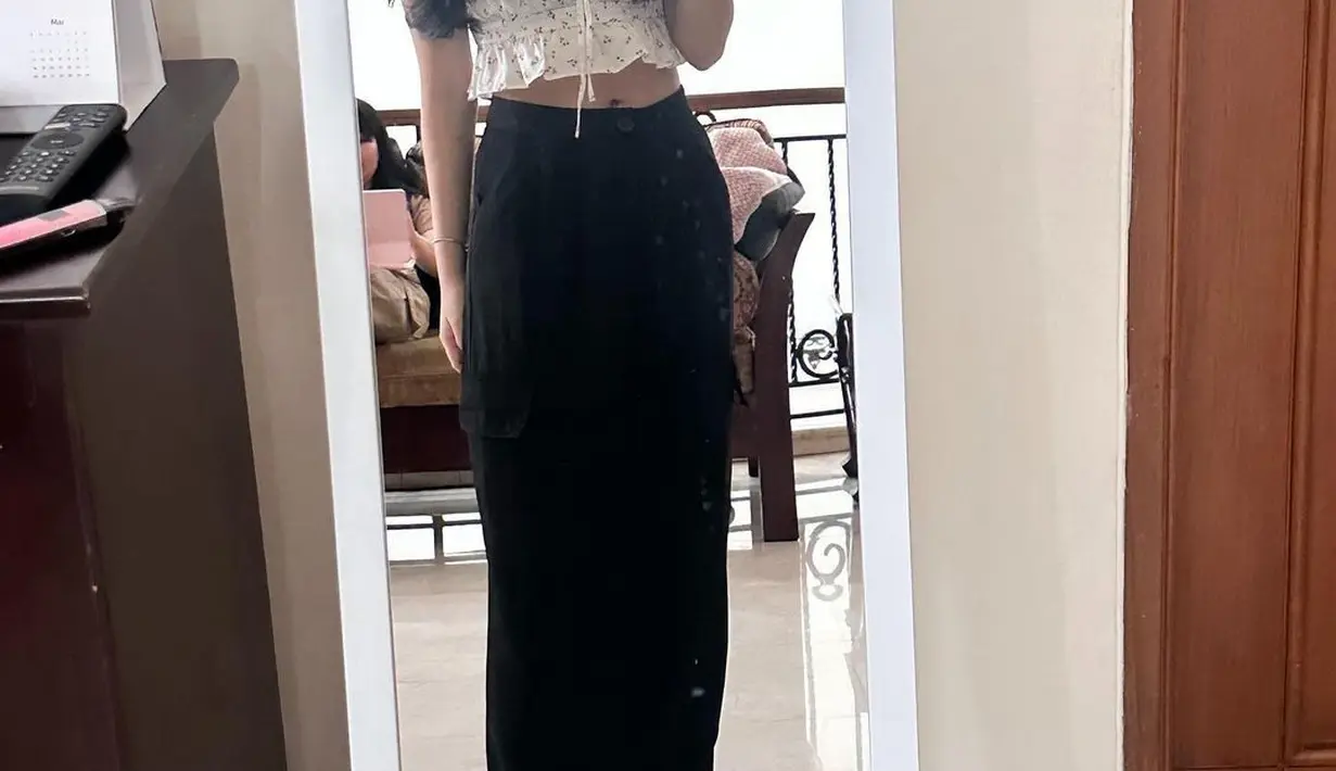 Potret mirror selfie Eca Aura mengenakan cropped top putih dengan detail kerut yang manis, dipadunya dengan rok panjang berwarna hitam. [Foto: Instagram/elsaajapasal]