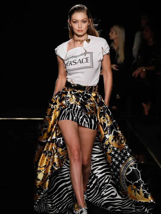 Model Gigi Hadid memperagakan busana koleksi Versace Pre-Fall 2019 di New York (2/12). Gigi tampil mengenakan t-shirt putih dengan logo Versace di bagian depan dipadukan dengan rok satin berwarna hitam, kuning dan putih. (AFP Photo/JP Yim)