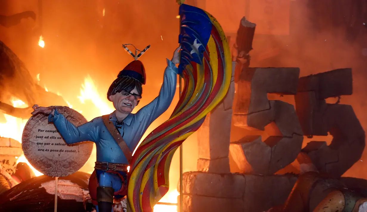 Sebuah karakter yang mewakili mantan presiden Catalan, Carles Puigdemont sedang memegang bendera Catalonia dibakar saat festival tradisional Fallas di Valencia, Spanyol (19/3). (AP/Alberto Saiz)