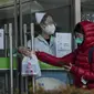 Seorang perempuan mengumpulkan kit antigen COVID-19 dari seorang pekerja di apotek di Beijing, Minggu (11/12/2022).  Sejumlah kota besar mulai membatalkan kendali antivirus dari kebijakan nol-Covid negara tersebut sejak pekan lalu karena protes massa. (AP Photo/Andy Wong)