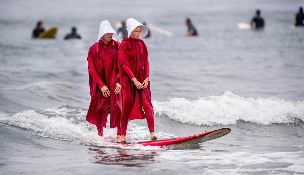 Erik dan April berselancar menggunakan kostum karakter dari The Handmade's Tale di Newport Beach, California, 28 Oktober 2017. Acara ini untuk merayakan Halloween yang jatuh pada tanggal 31 Oktober. (Paul Rodriguez/The Orange County Register via AP)