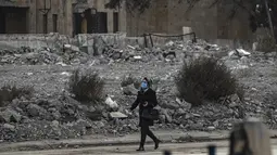 Seorang perempuan mengenakan masker berjalan melewati puing-puing di kota Raqa, bekas ibu kota ISIS, di Suriah utara pada 20 Desember 2020. Raqqa menjadi saksi terusirnya anggota kelompok ekstremis oleh Pasukan Demokratik Suriah pada Oktober 2017 lalu. (Photo by Delil SOULEIMAN / AFP)