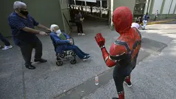 Seseorang yang mengenakan kostum Spiderman menyapa seorang wanita di atas kursi roda setelah disuntik vaksin covid-19 Pfizer-BioNTech di Mexico City, Meksiko, Selasa (28/12/2021). Spiderman tersebut dipekerjakan oleh Pemerintah Kota untuk menghibur para peserta vaksinasi. (ALFREDO ESTRELLA / AFP)