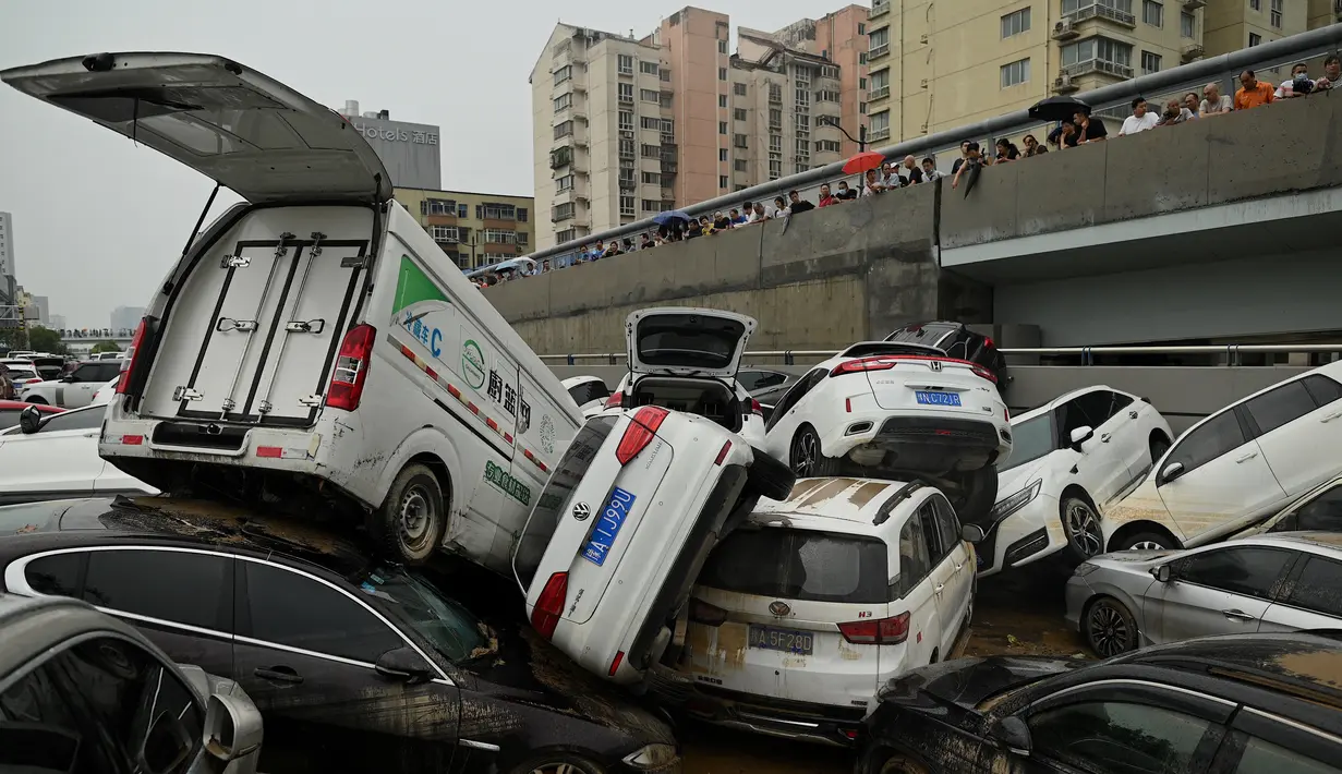 Orang-orang melihat mobil-mobil yang terendam banjir setelah hujan lebat melanda Zhengzhou di provinsi Henan, China, Kamis (22/7/2021). Para peramal cuaca mengatakan Zhengzhou mendapat curah hujan dalam setahun hanya dalam tiga hari. (Noel Celis/AFP)