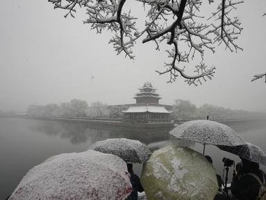 Pengunjung berkerumun untuk mengambil foto di tempat yang indah untuk Kota Terlarang saat salju turun di Beijing, China (18/3/2022). Gelombang dingin melanda banyak bagian China, menyebabkan suhu turun dan mengganggu lalu lintas di daerah yang terkena dampak. (AP Photo/Ng Han Guan)