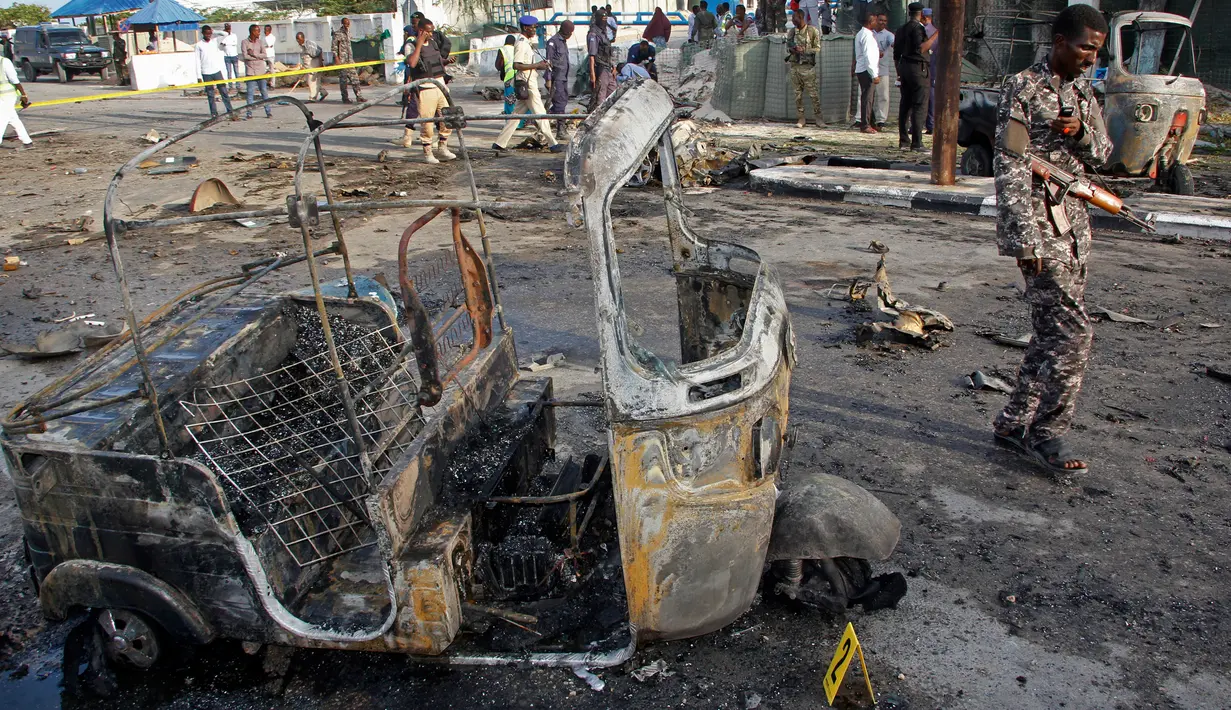 Tentara Somalia melewati puing kendaraan di lokasi ledakan bom mobil dekat pos pemeriksaan parlemen dan Kementerian Dalam Negeri di Mogadishu, Minggu (25/3). Ledakan terjadi di kawasan yang dijaga dengan sangat ketat di kota itu. (AP/Farah Abdi Warsameh)