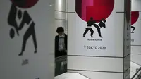 Seorang pria yang mengenakan masker pelindung untuk mencegah penyebaran virus corona berjalan di depan iklan Olimpiade Tokyo 2020 di Tokyo, Rabu (17/3/2021). Ibukota Jepang mengonfirmasi lebih dari 400 kasus virus korona baru pada hari Rabu. (AP Photo/Eugene Hoshiko)