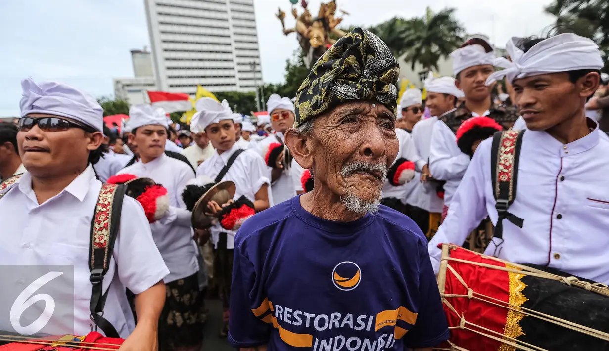 Seorang kakek dari simpatisan Partai NasDem mengikuti pawai ogoh-ogoh saat aksi Kita Indonesia di Bundaran HI, Jakarta, Minggu (04/12). Aksi tersebut adalah acara perayaan kegembiraan atas keberagaman dan kebangsaan Indonesia. (Liputan6.com/Fery Pradolo)