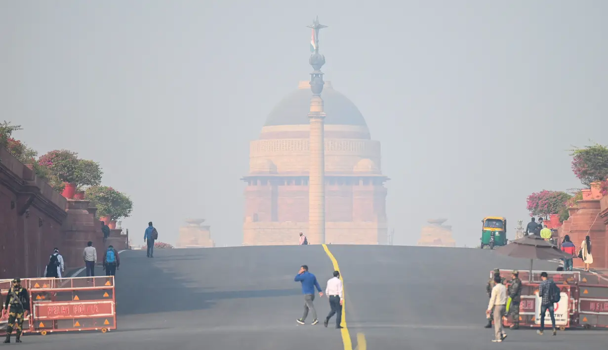 Orang-orang berjalan di dekat istana kepresidenan di tengah kondisi kabut asap tebal di New Delhi (15/11/2021). Otoritas kota New Delhi tengah mempertimbangkan penguncian wilayah akibat kian memburuknya polusi udara. (AFP/Money Sharma)