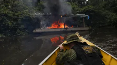 Petugas lingkungan Brasil saat berlindung dari kapal yang dibakar selama operasi terhadap penambangan emas ilegal di perairan hutan hujan Amazon, Roraima, Brasil (16/4). Daerah ini merupakan tempat dimana suku Yanomami tinggal. (REUTERS / Bruno Kelly)