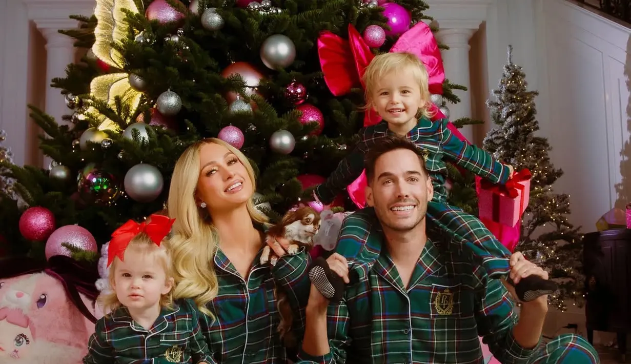 Paris Hilton bersama suami dan kedua anaknya berfoto di depan pohon Natal dengan hiasan kupu-kupu. Keluarga ini pun tampil dengan piyama hijau motif kotak-kotak. [@parishilton]